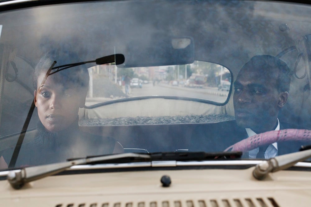 Two people seen through a car windscreen, the passenger gazing out to the side
