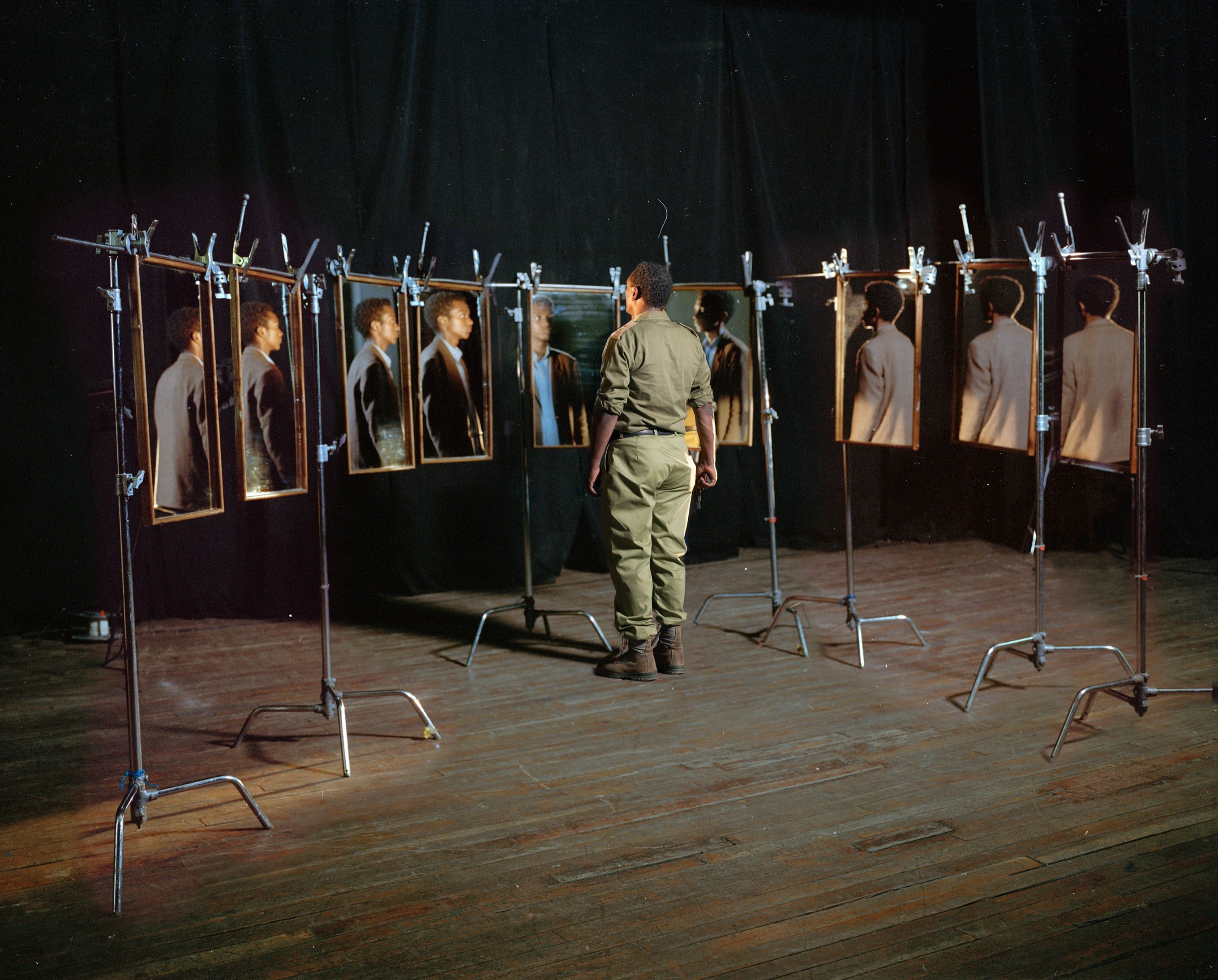 Installation view: portrait photographs mounted on stands in a darkened room, a man in uniform standing among them