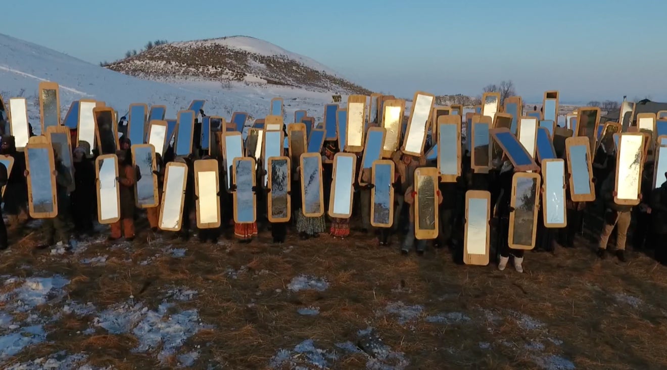 A line of Water Protectors holding mirrored shields in front of a snowy hill at Standing Rock