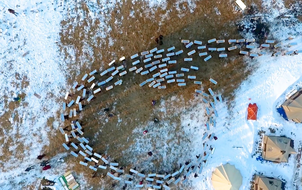 Aerial view of Water Protectors carrying mirrored shields in a serpent formation across snowy ground at Standing Rock