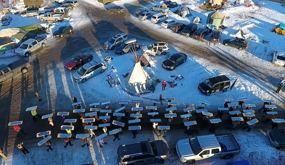 Aerial view of mirrored shields laid out in rows among parked cars in the snowy camp